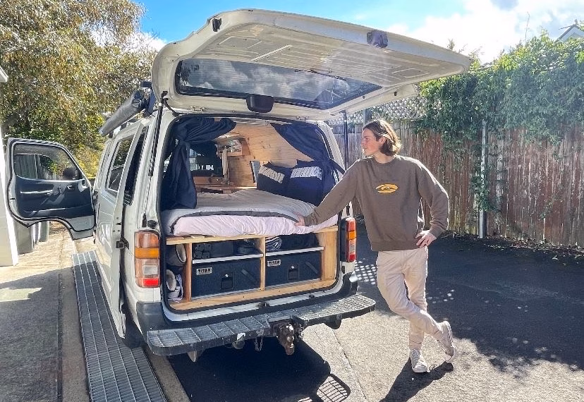 Flynn Batterham standing next to his van with a bed inside.