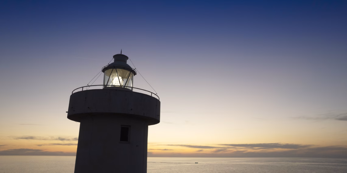 A lighthouse at sunset with a light shining.