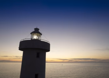 A lighthouse at sunset with a light shining.
