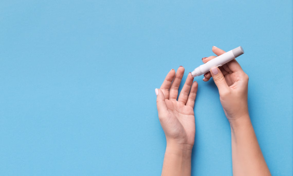 Diabetes test. Woman hands checking blood sugar level by Glucose meter on blue background, copy space