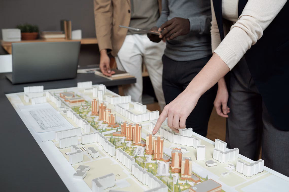 Hand of female architect pointing at layout during presentation of architectural project to male coworkers