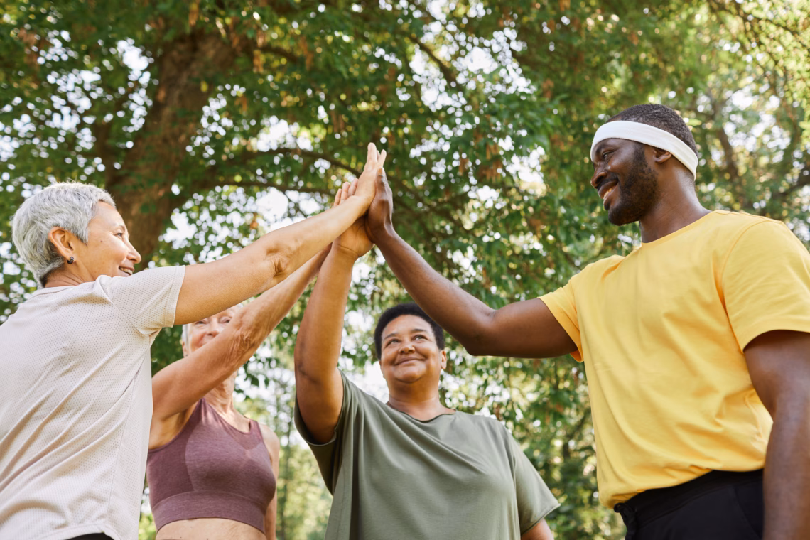 Low angle view at group of active senior women high five with male trainer after enjoying outdoor workout