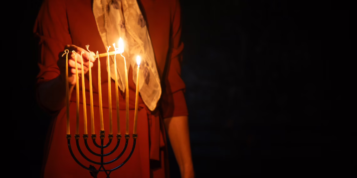 A woman in a red dress lighting the candles of a Menorah in a dimly lit room, symbolizing the Chanukah services attended by the Member for Bradfield.