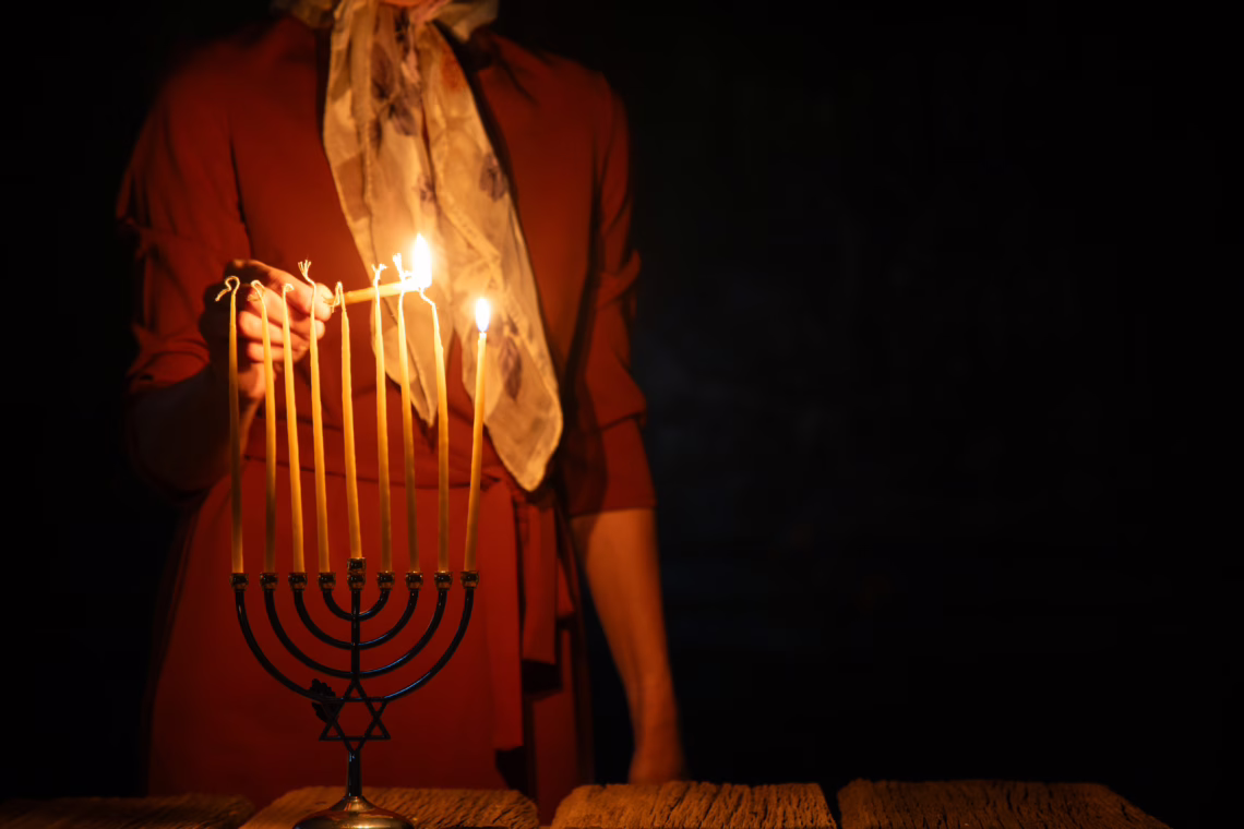 A woman in a red dress lighting the candles of a Menorah in a dimly lit room, symbolizing the Chanukah services attended by the Member for Bradfield.