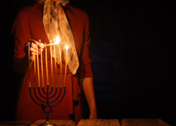 A woman in a red dress lighting the candles of a Menorah in a dimly lit room, symbolizing the Chanukah services attended by the Member for Bradfield.